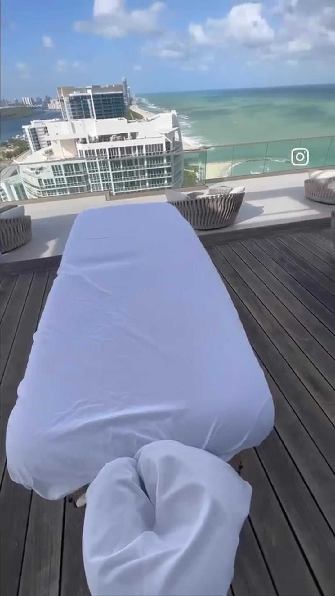 A massage table dressed in white linens on a deck above the ocean