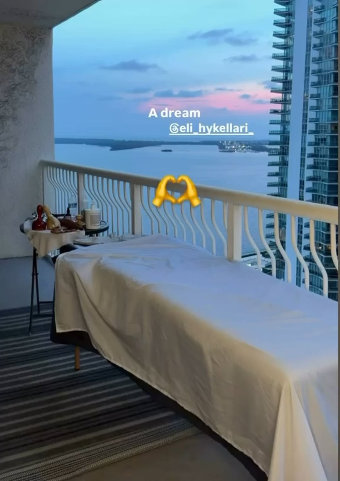 A massage table set up on a balcony overlooking the water at sunset